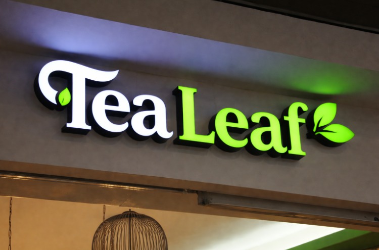Illuminated storefront sign reading "TeaLeaf" with white and bright green lettering, featuring small leaf graphics on each word.