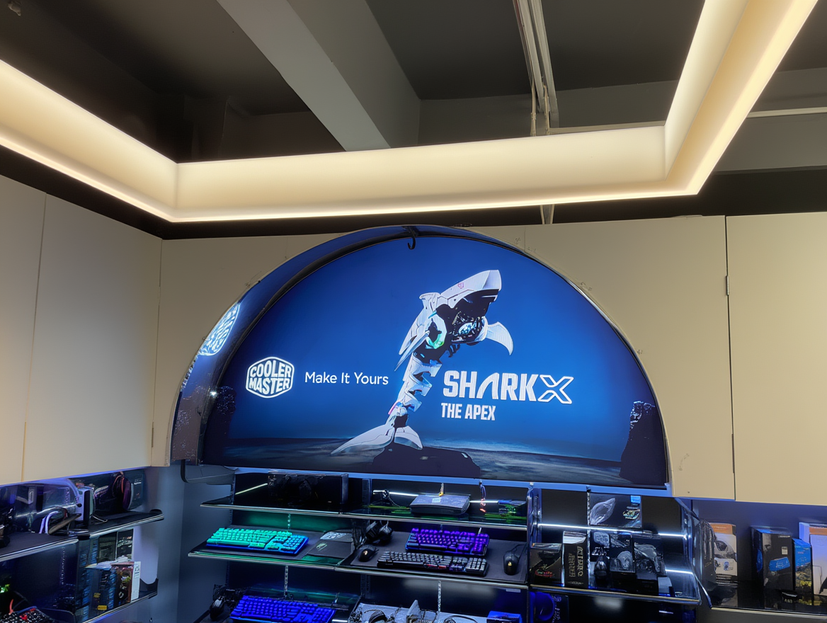 A gaming store display features a Cooler Master SHARK X The Apex sign above shelves with computer keyboards, mice, and accessories.